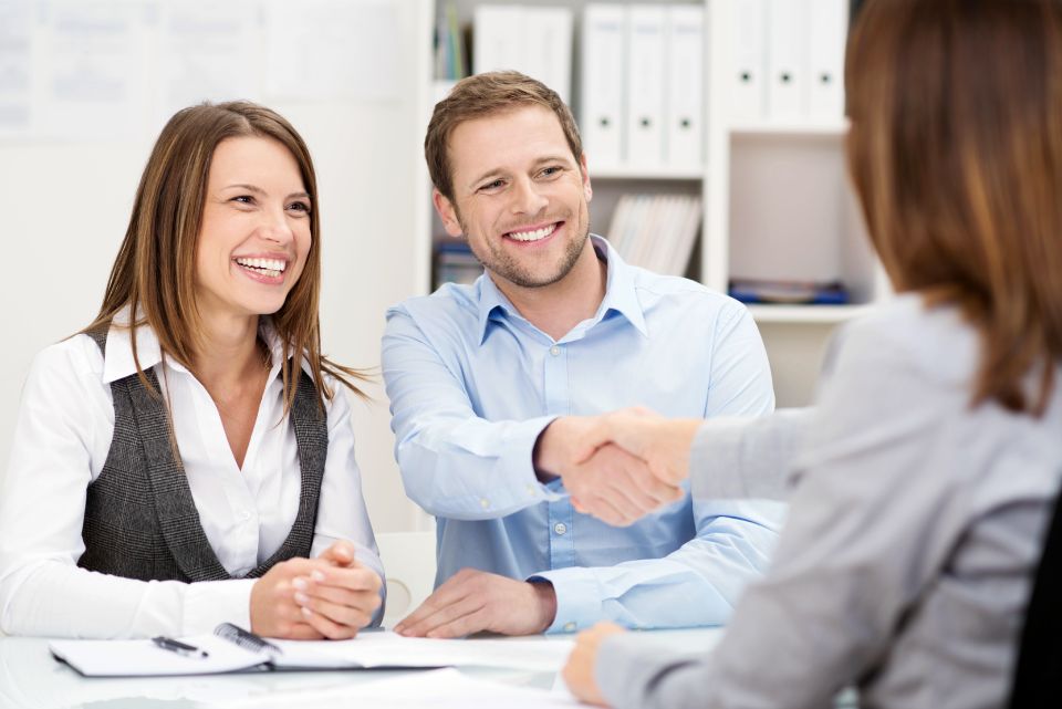 A couple in an office is handshaking with an office manager.